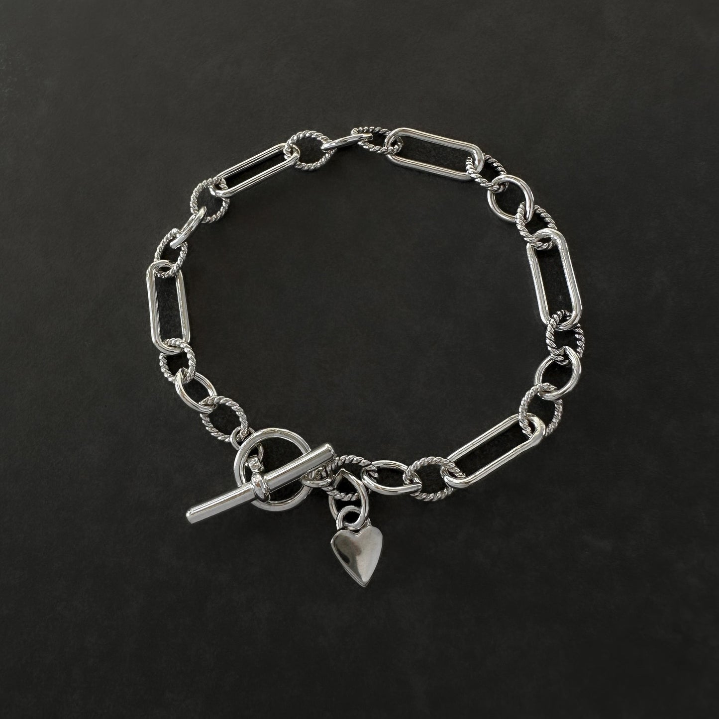 Silver chain bracelet with a heart charm on a dark background