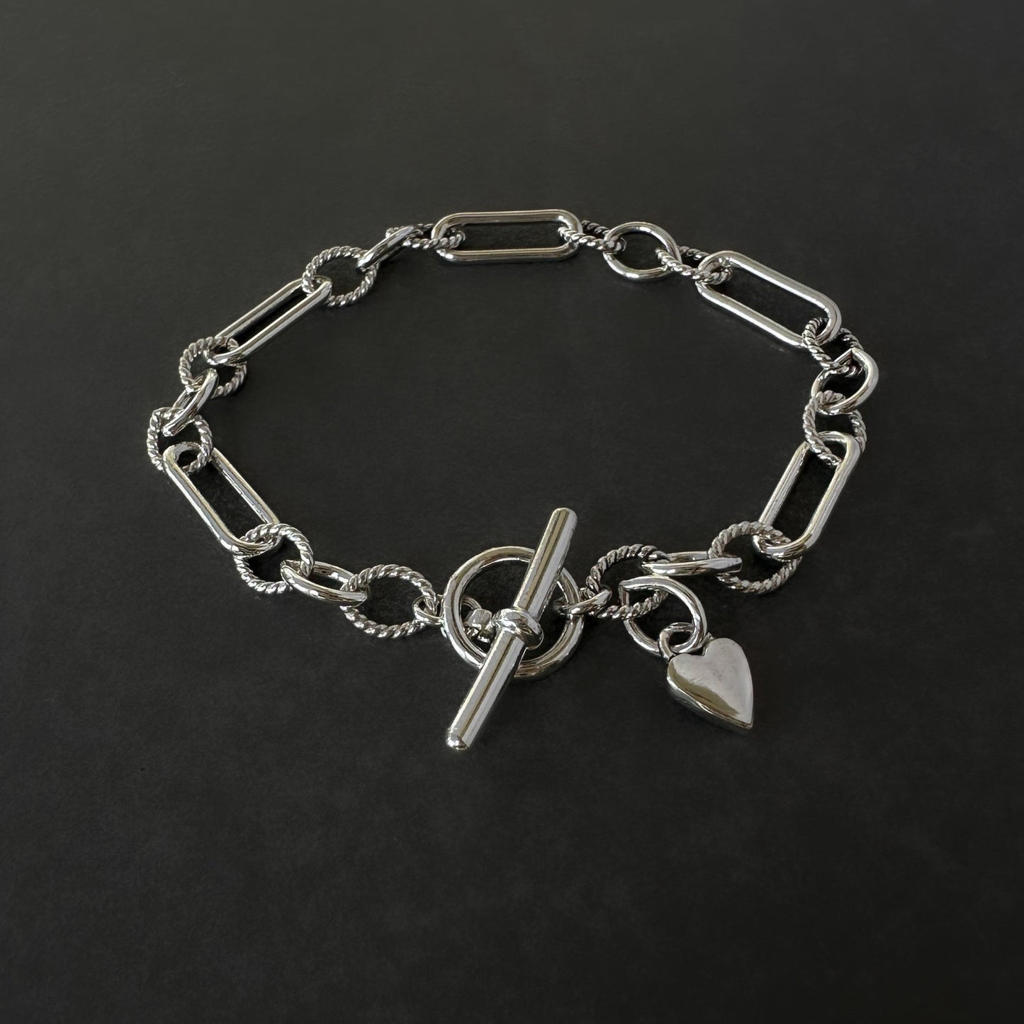 Silver chain bracelet with a toggle clasp and heart charm on a black background