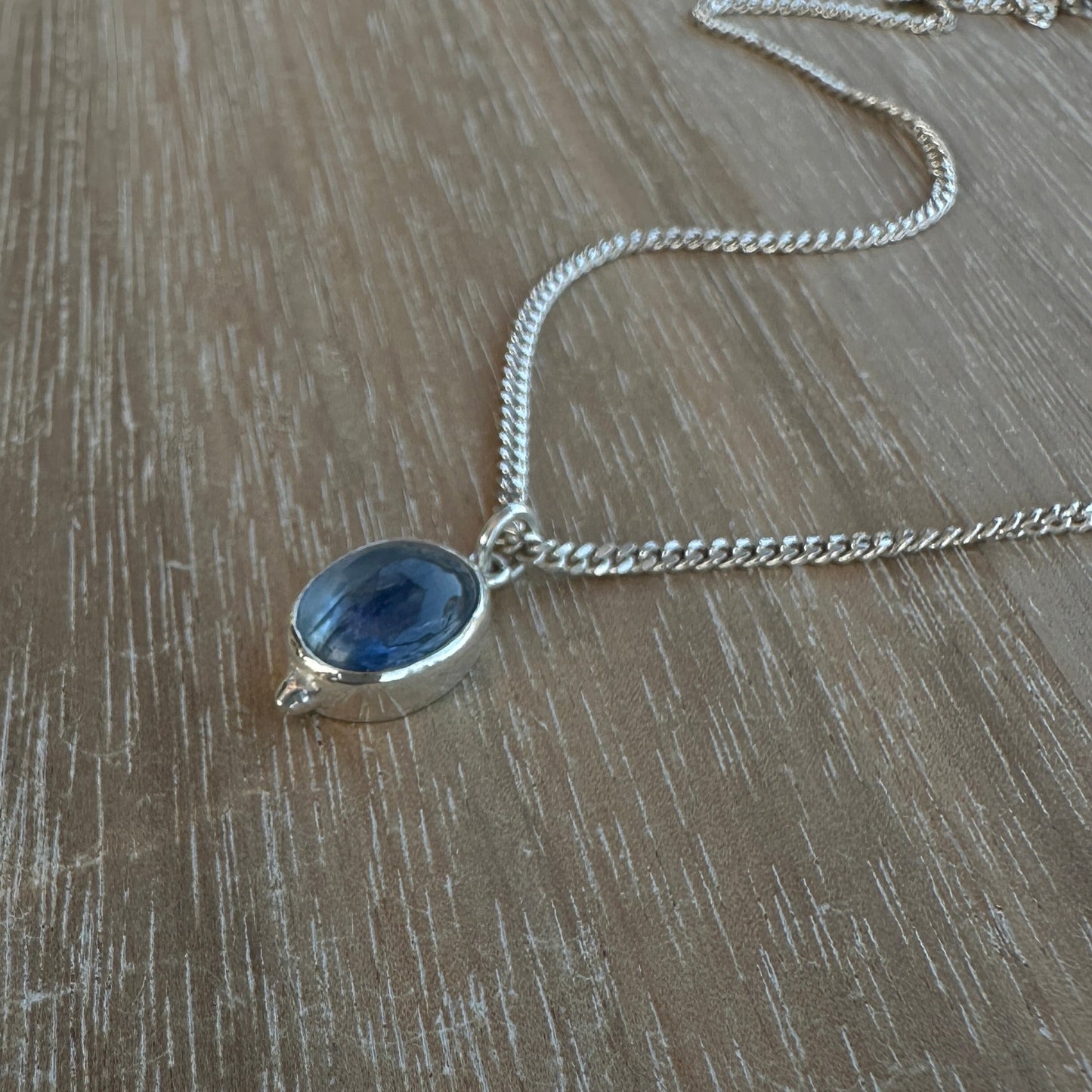 Silver necklace with a blue pendant on a wooden surface