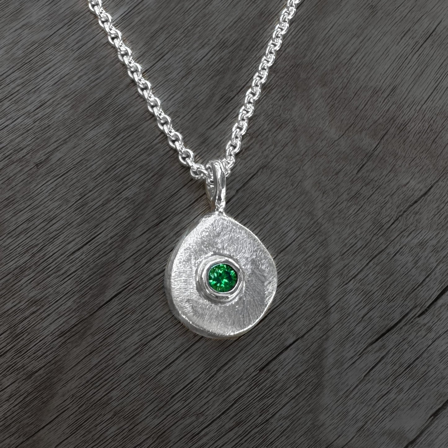 Silver necklace with a round pendant featuring a green gemstone on a wooden surface