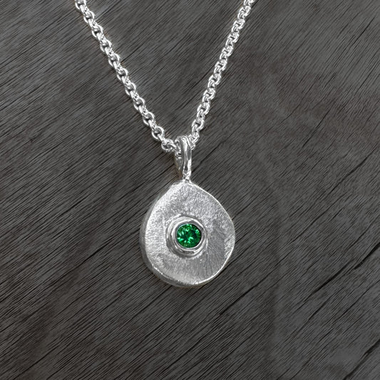 Silver necklace with a round pendant featuring a green gemstone on a wooden surface