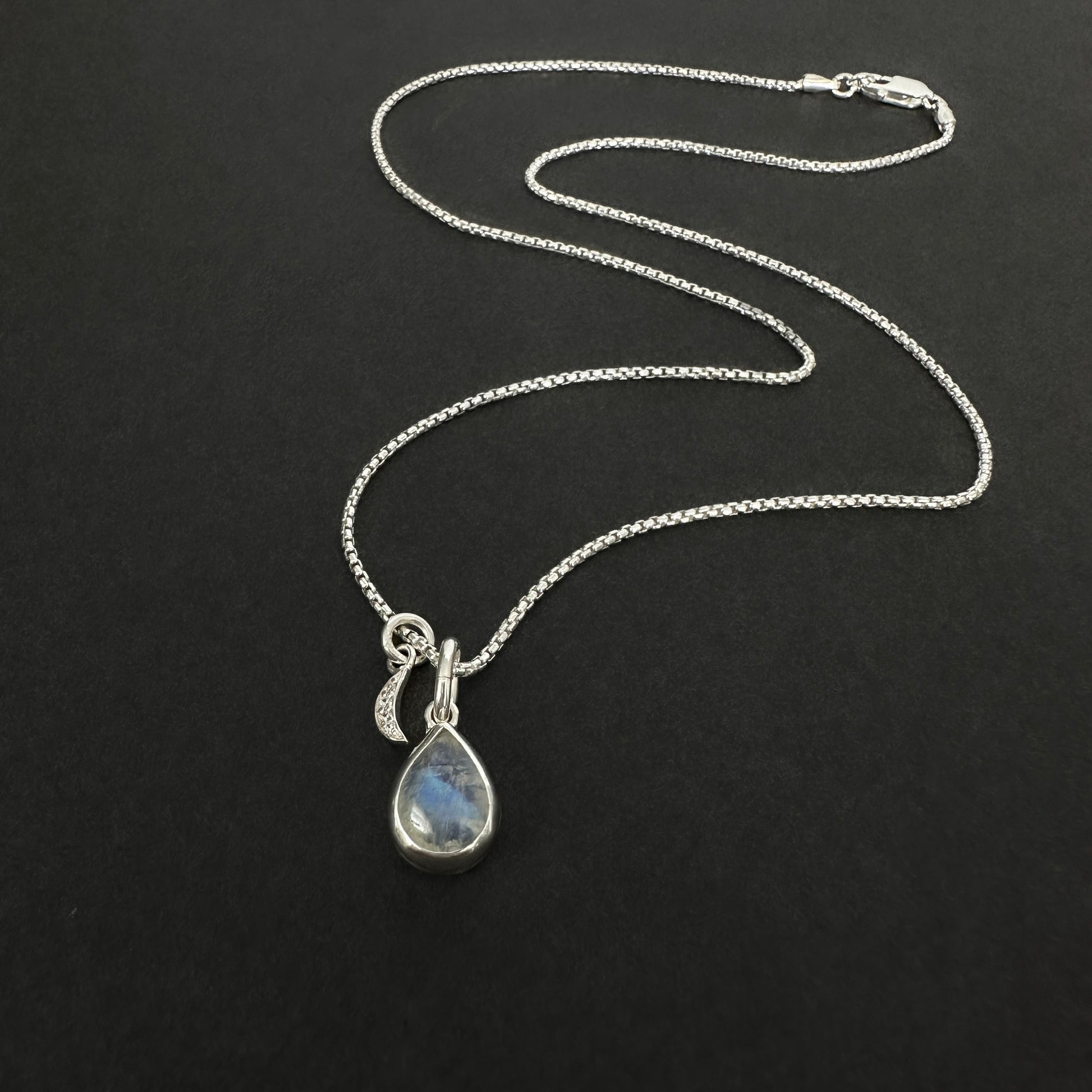 Silver necklace with a teardrop-shaped pendant on a black background