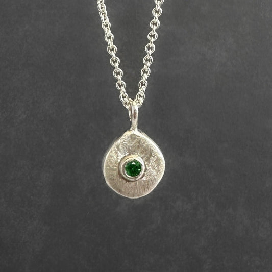 Silver necklace with a round pendant featuring a green gemstone on a dark gray background