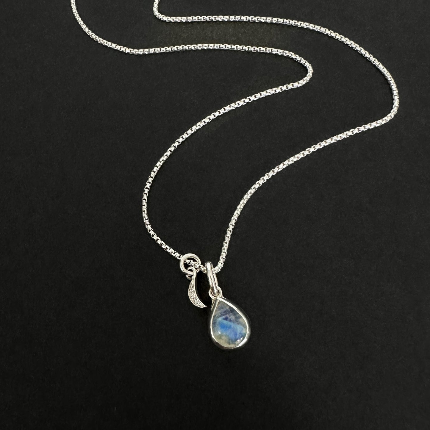 Silver necklace with a teardrop-shaped pendant on a black background