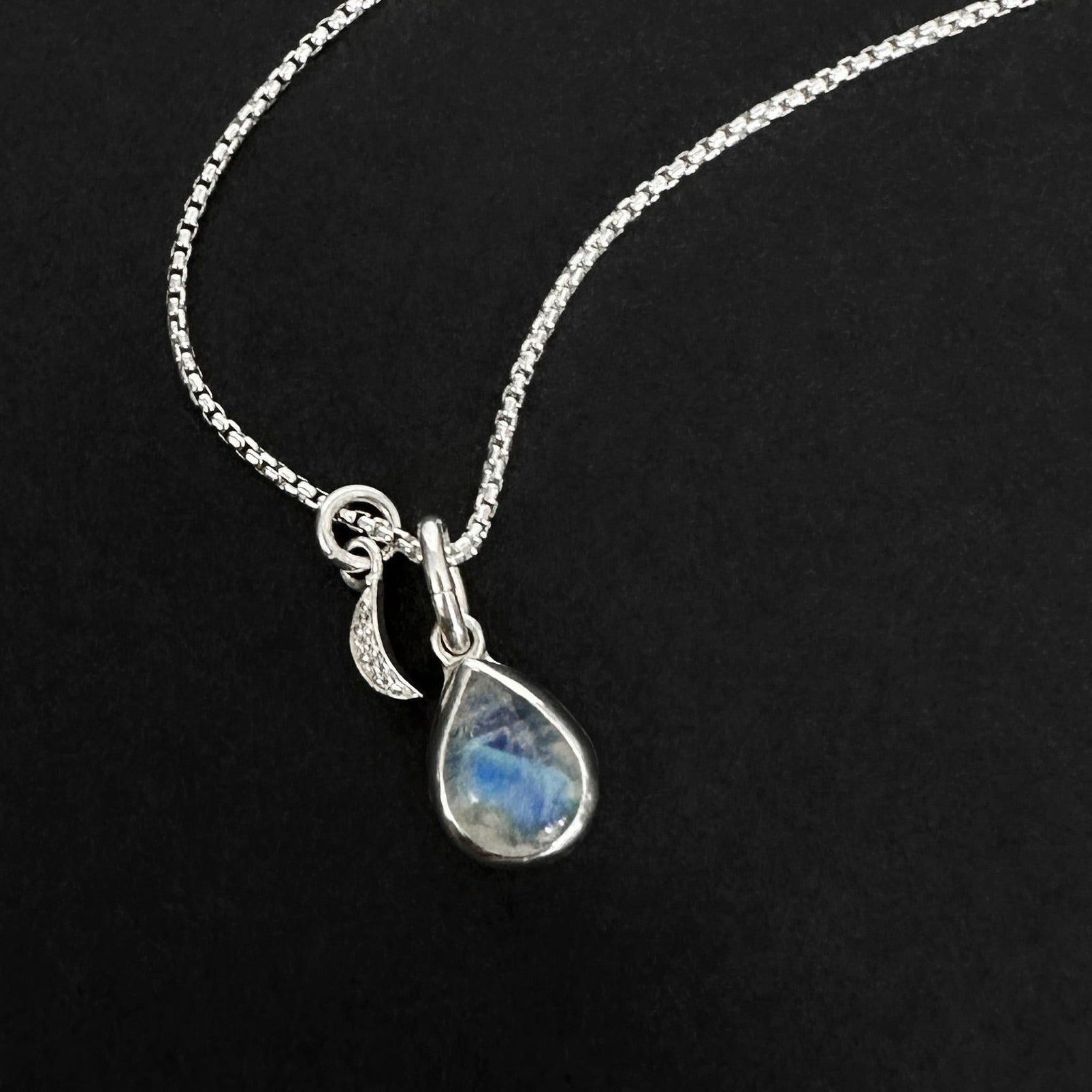 Silver necklace with a teardrop-shaped moonstone pendant on a black background