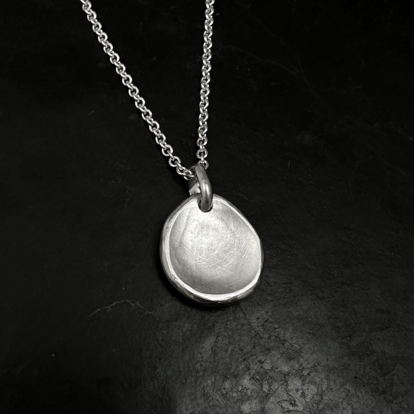 Silver necklace with a round pendant on a dark textured surface