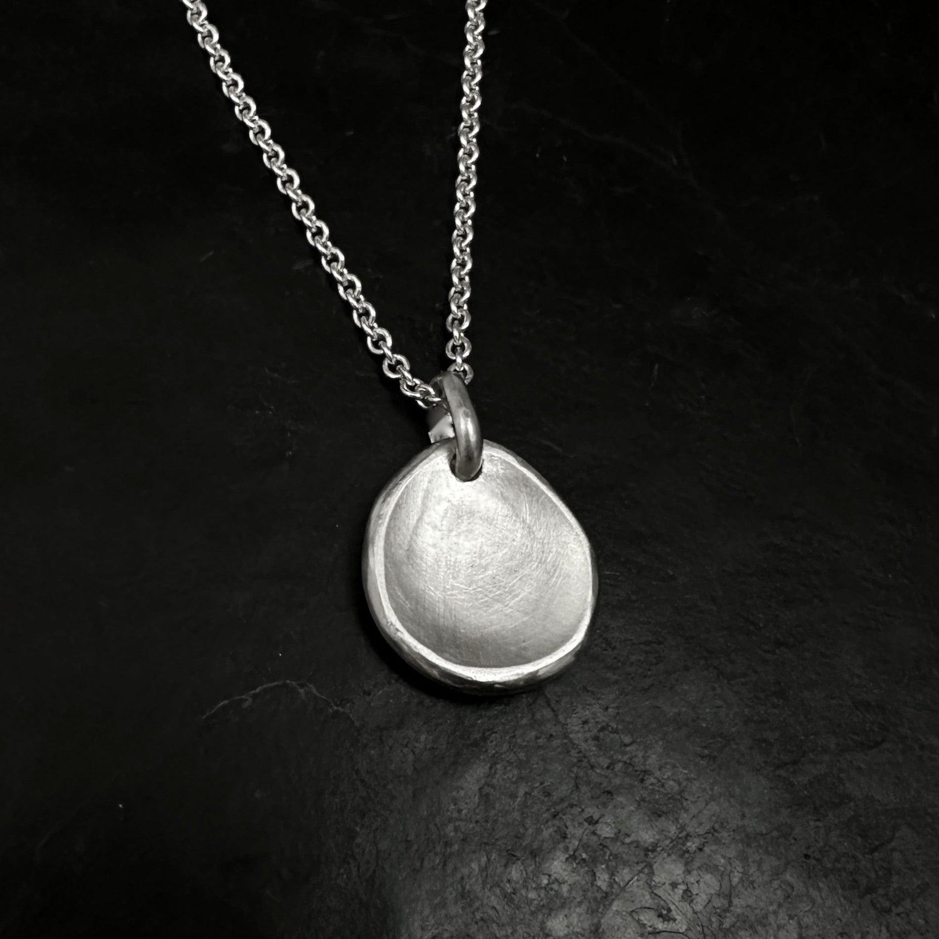 Silver necklace with a round pendant on a dark textured surface