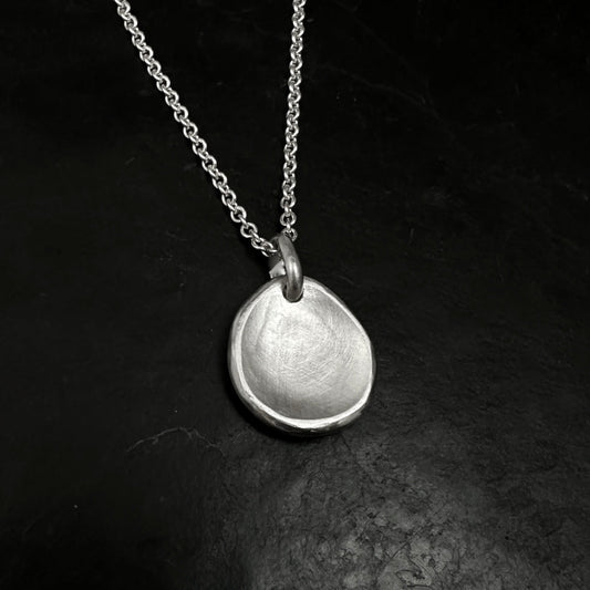 Silver necklace with a round pendant on a dark textured surface