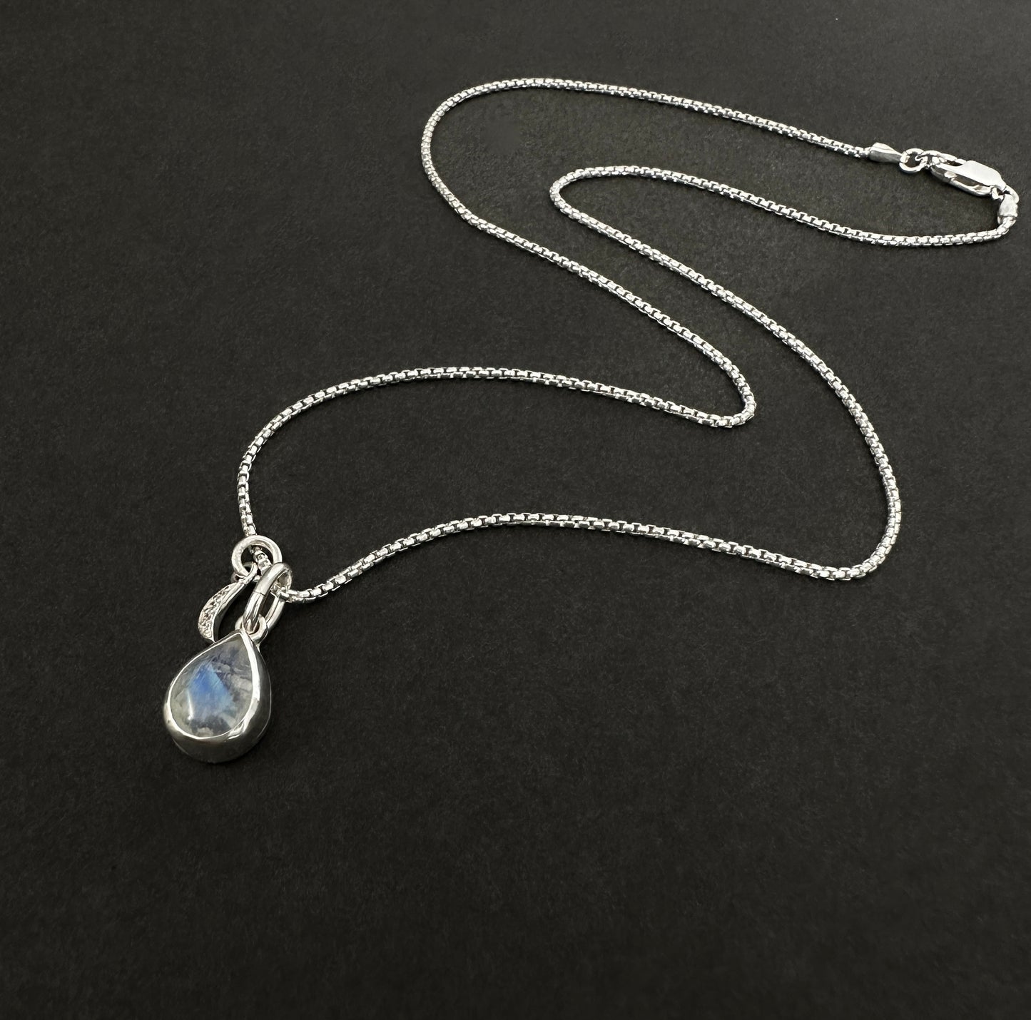 Silver necklace with a teardrop-shaped pendant on a black background