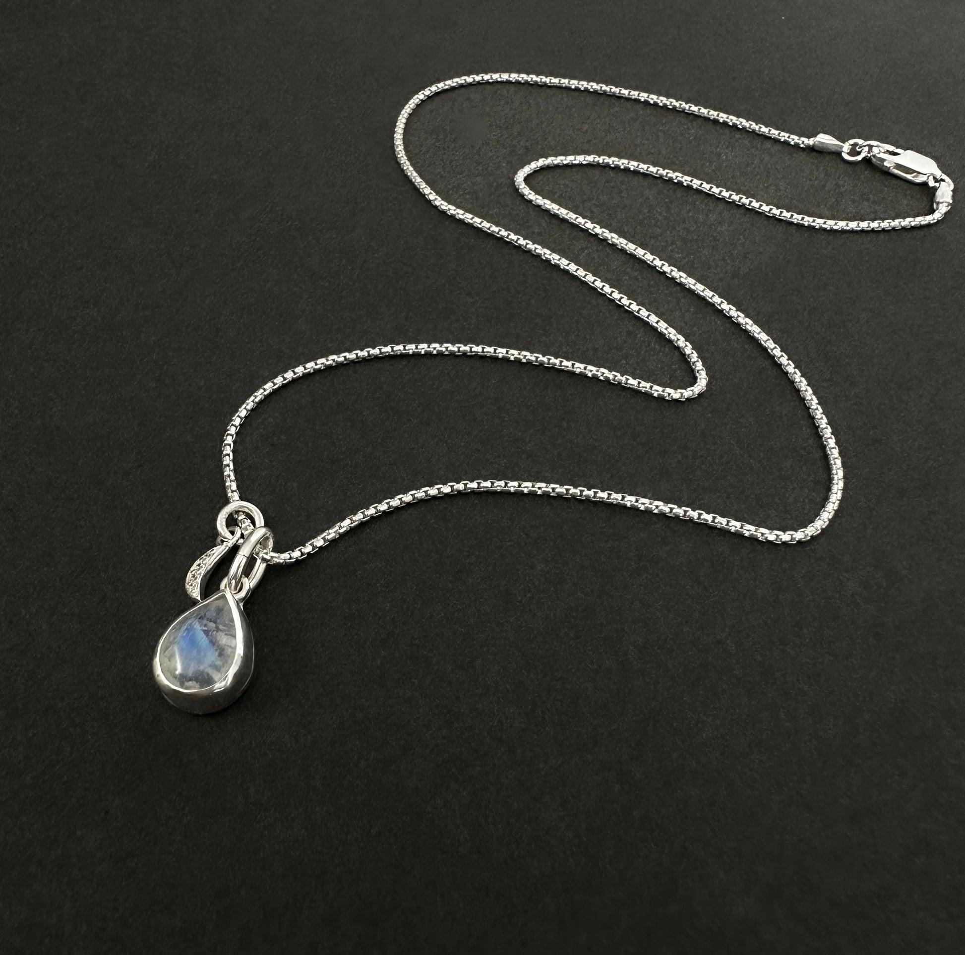 Silver necklace with a teardrop-shaped pendant on a black background