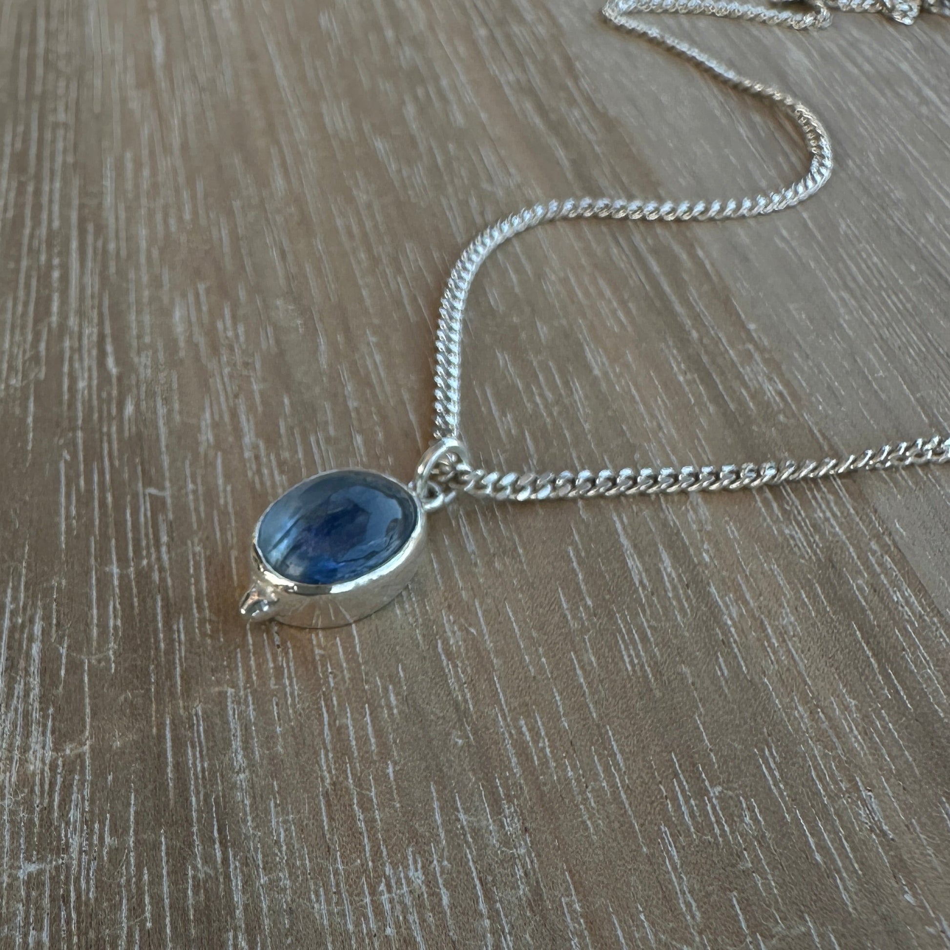 Silver necklace with a blue pendant on a wooden surface
