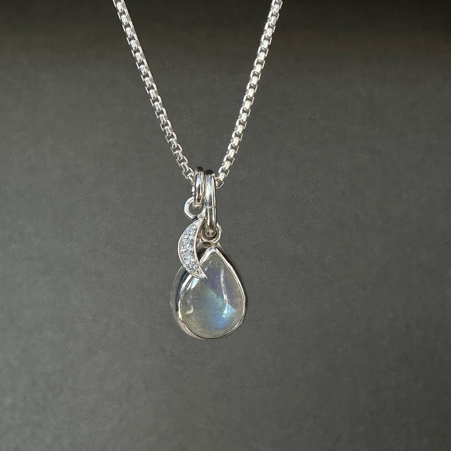 Silver necklace with a teardrop-shaped pendant on a dark gray background