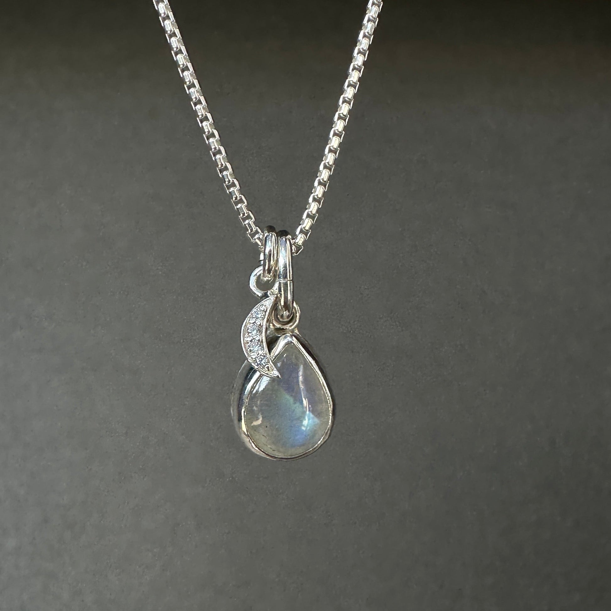 Silver necklace with a teardrop-shaped pendant on a dark gray background