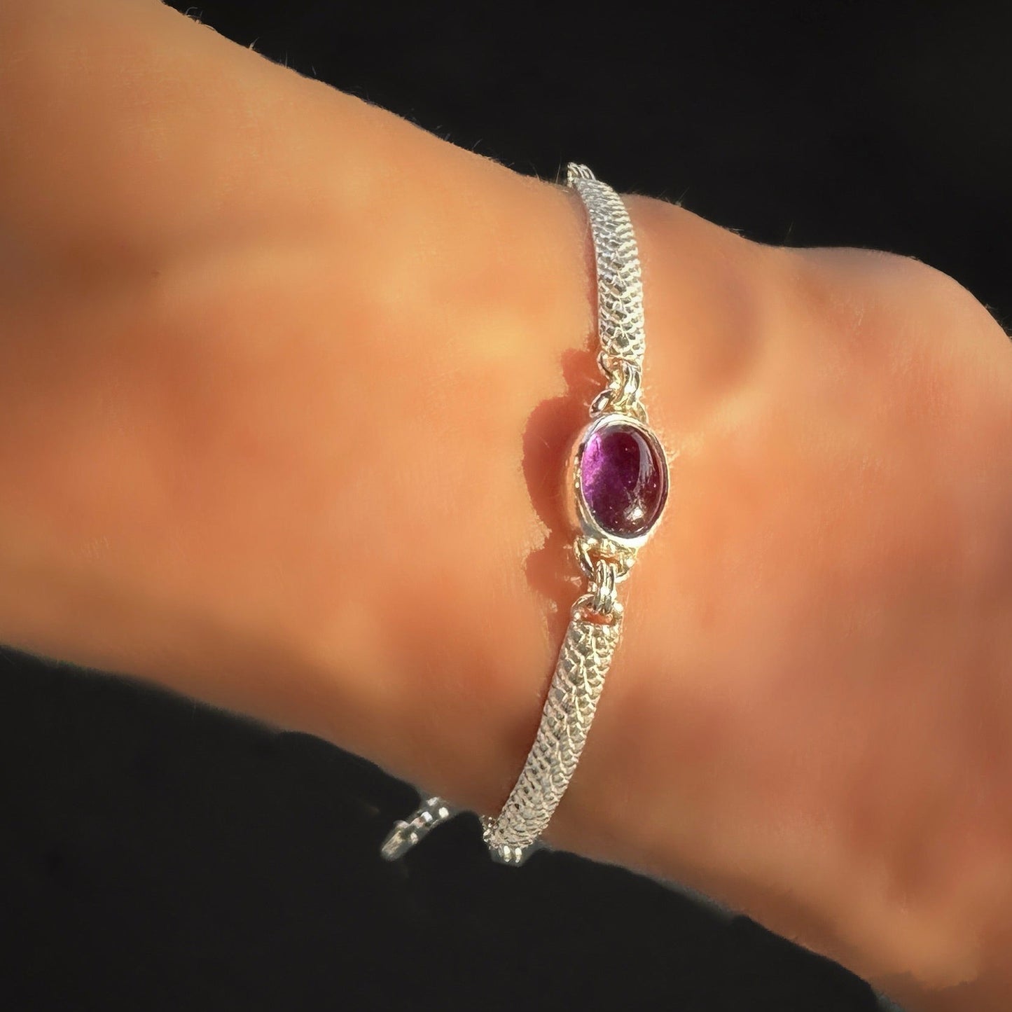 Silver bracelet with a purple gemstone on a wrist against a black background