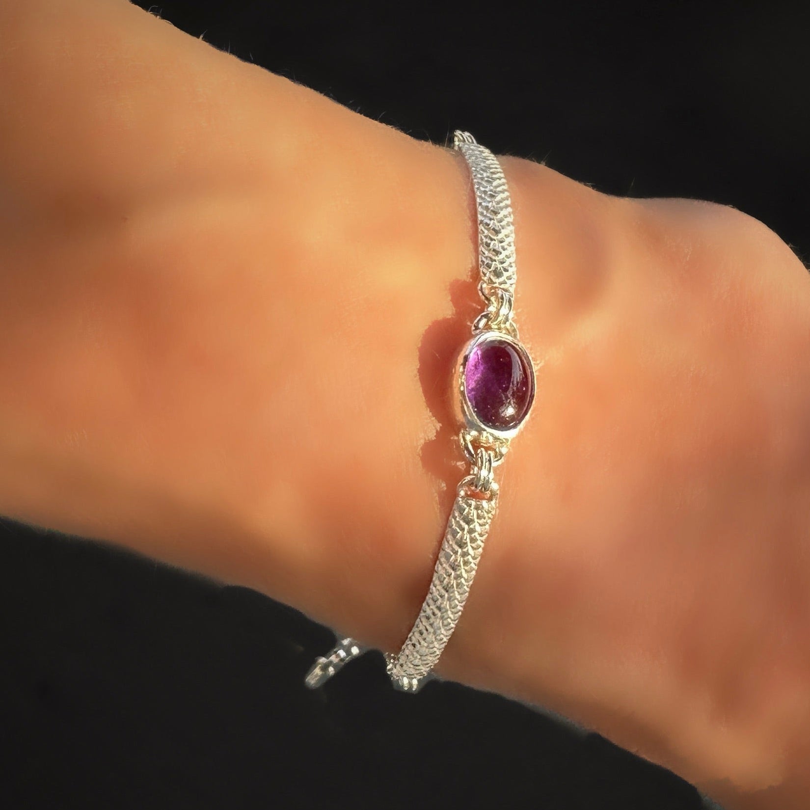 Silver bracelet with a purple gemstone on a wrist against a black background