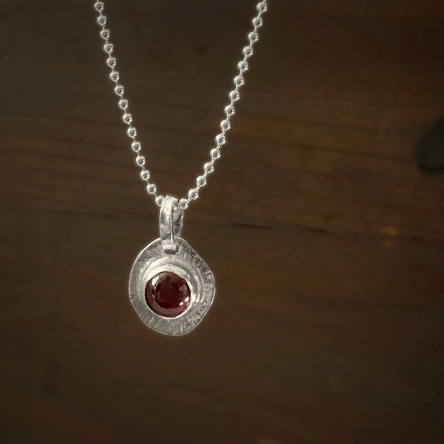 Silver necklace with a round pendant featuring a garnet gemstone on a dark wooden background