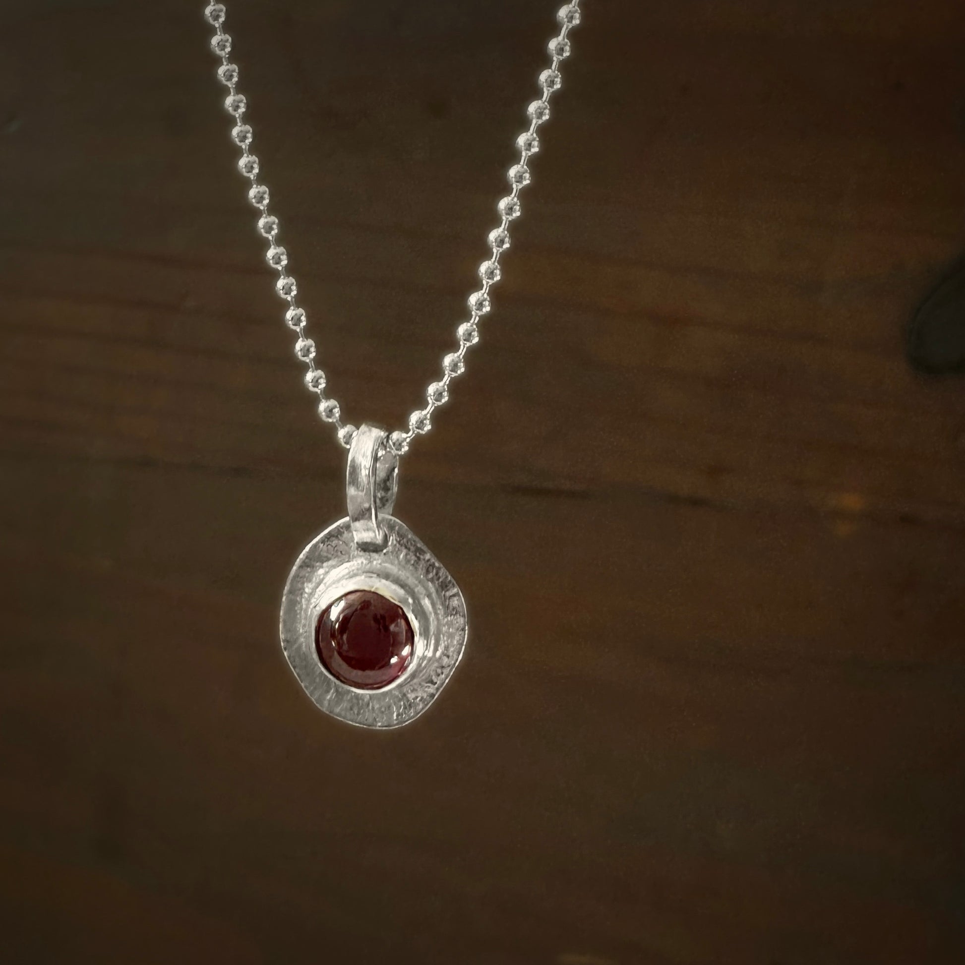 Silver necklace with a round pendant featuring a garnet gemstone on a dark wooden background