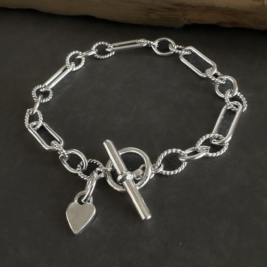 Silver chain bracelet with a heart charm and toggle clasp on a dark surface