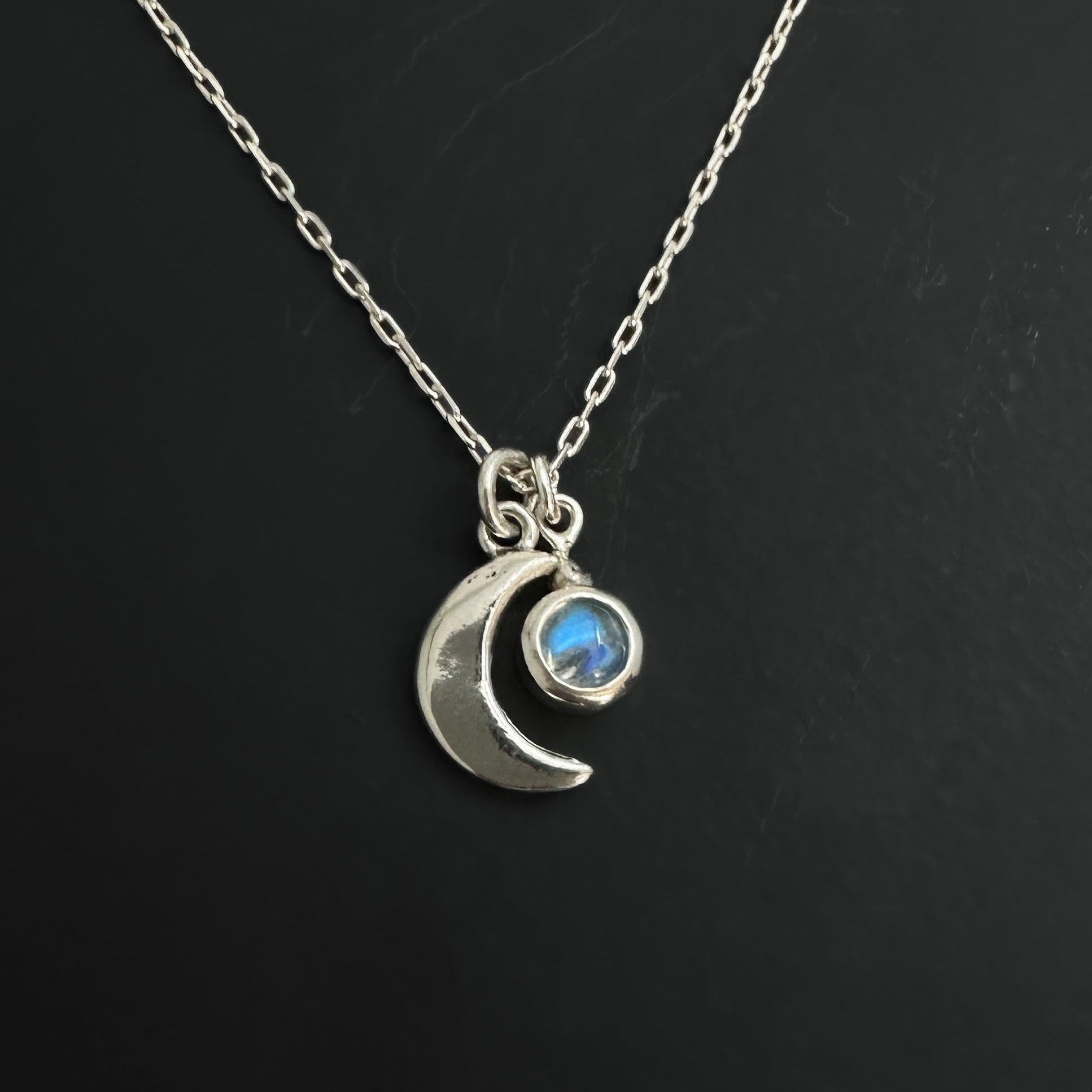 Silver necklace with a crescent moon and rainbow moonstone gemstone pendant on a black background