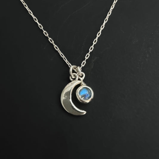 Silver necklace with a crescent moon and rainbow moonstone gemstone pendant on a black background