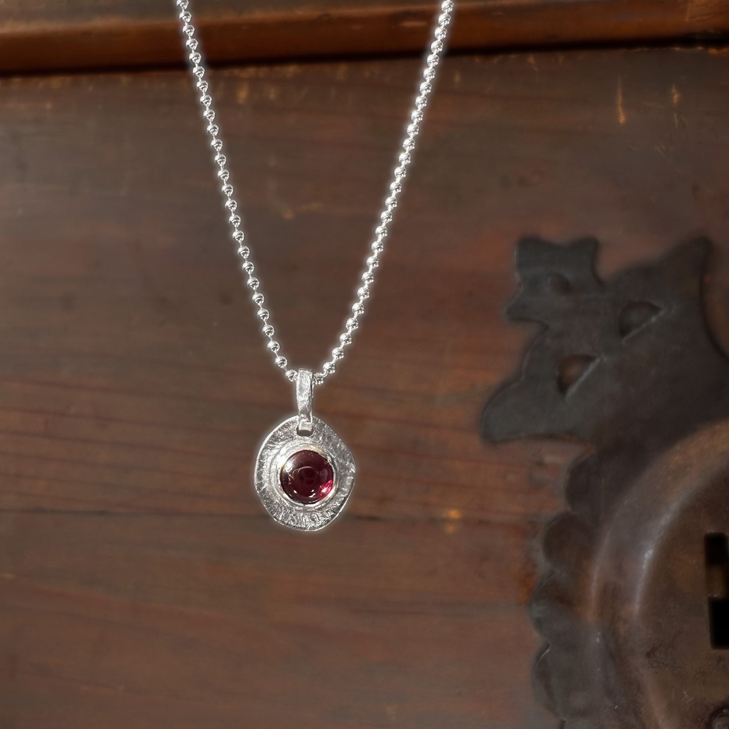 Silver necklace with a red gemstone pendant on a wooden surface