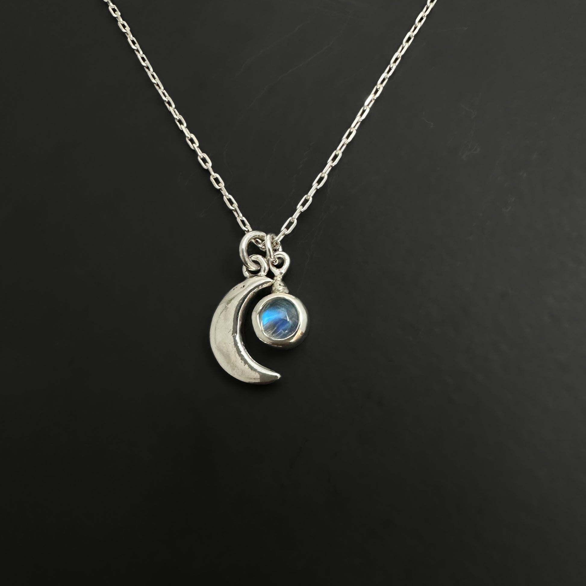 Silver necklace with a crescent moon pendant on a black background