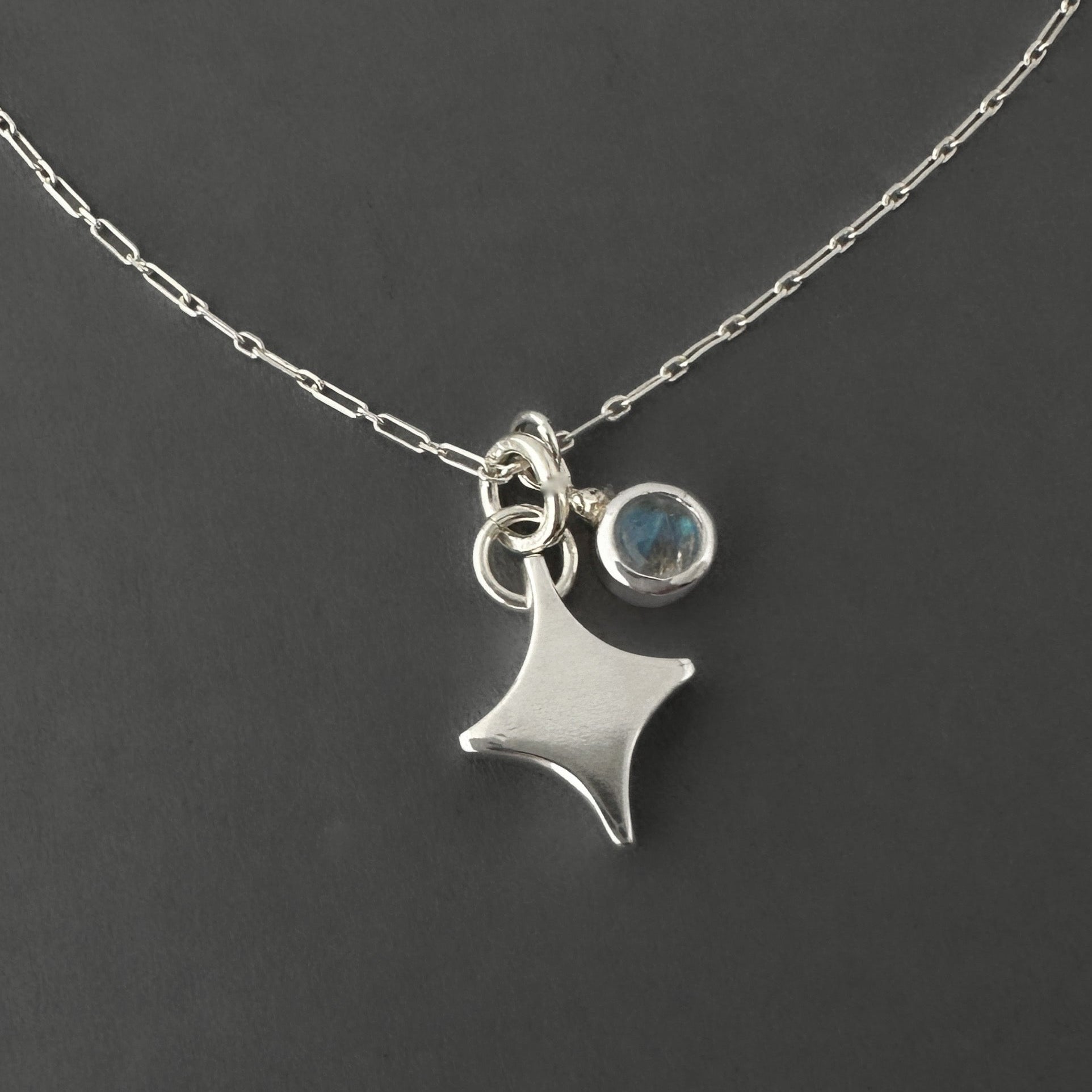 Silver necklace with a note star-shaped pendant and rainbow moonstone round charm on a dark background