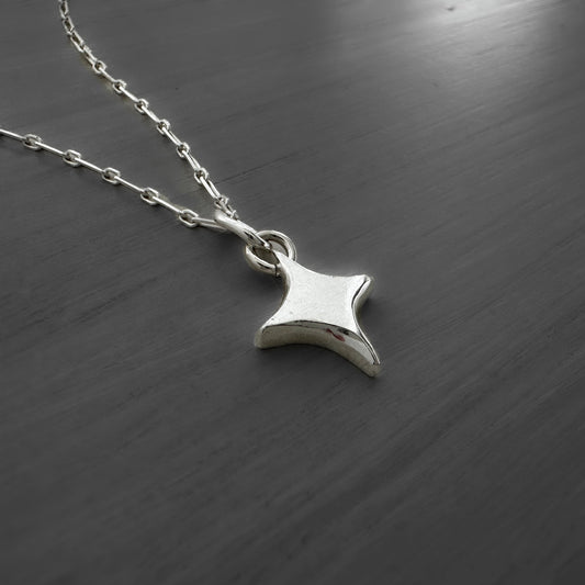 Silver star-shaped pendant on a chain against a dark wooden background