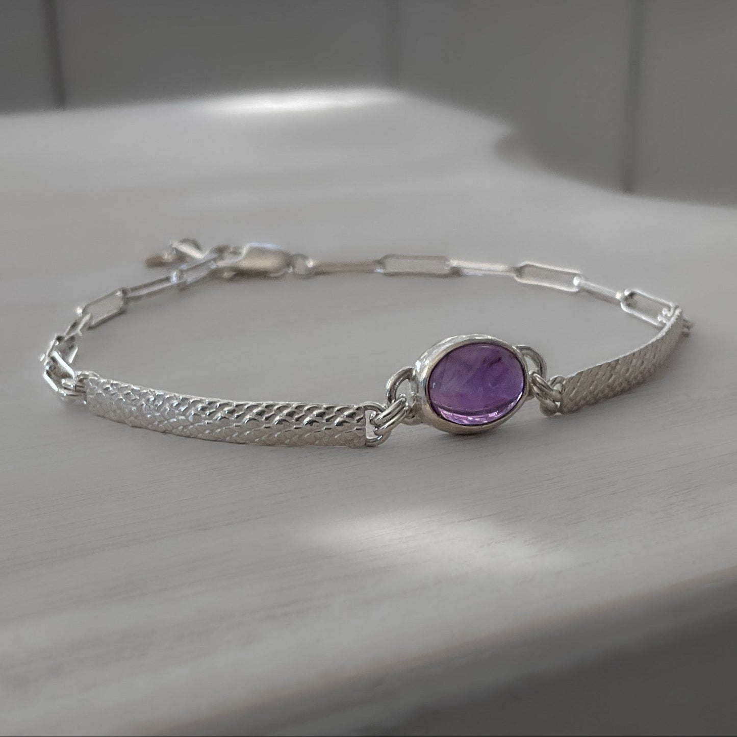 Silver bracelet with a purple gemstone on a light wooden surface