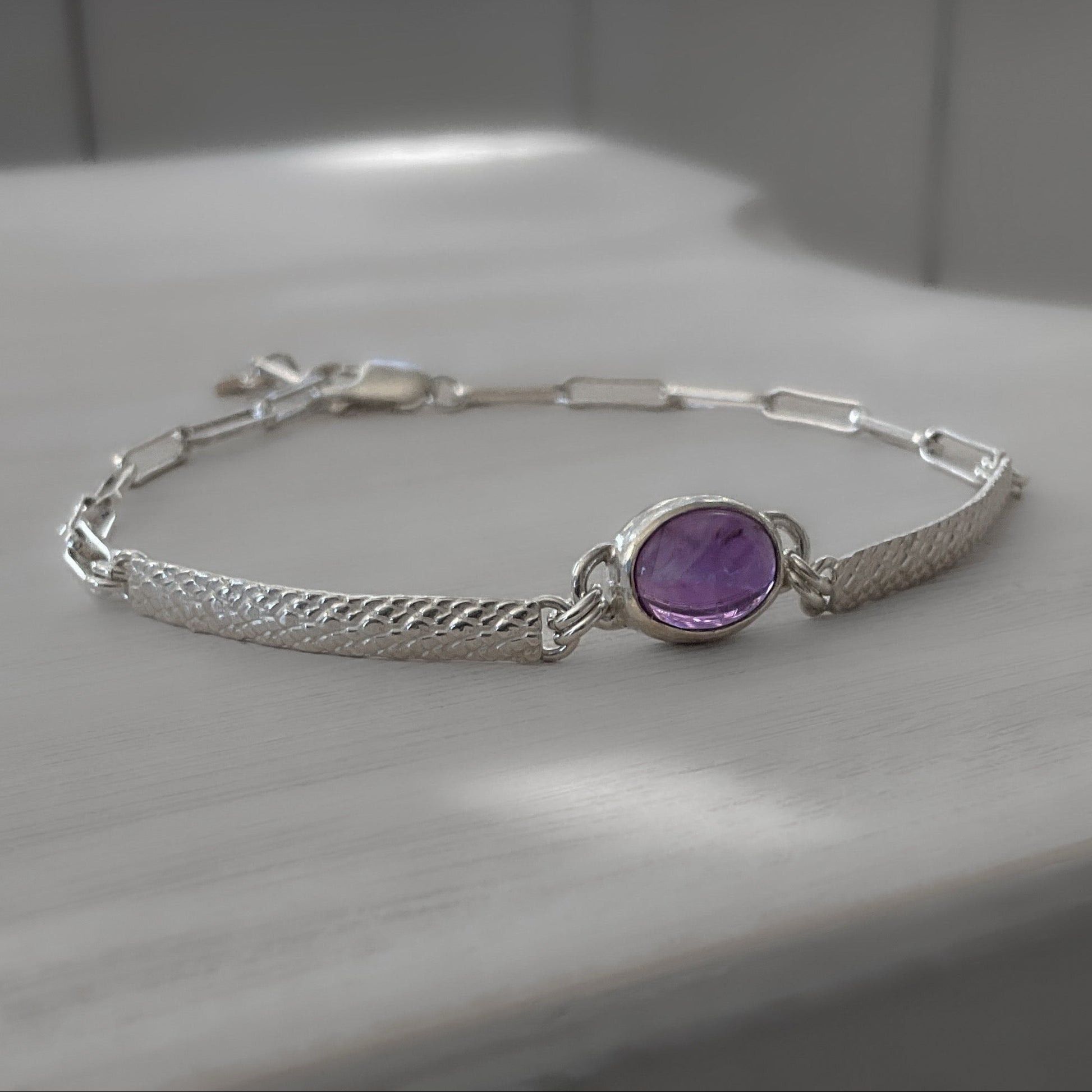 Silver bracelet with a purple gemstone on a light wooden surface