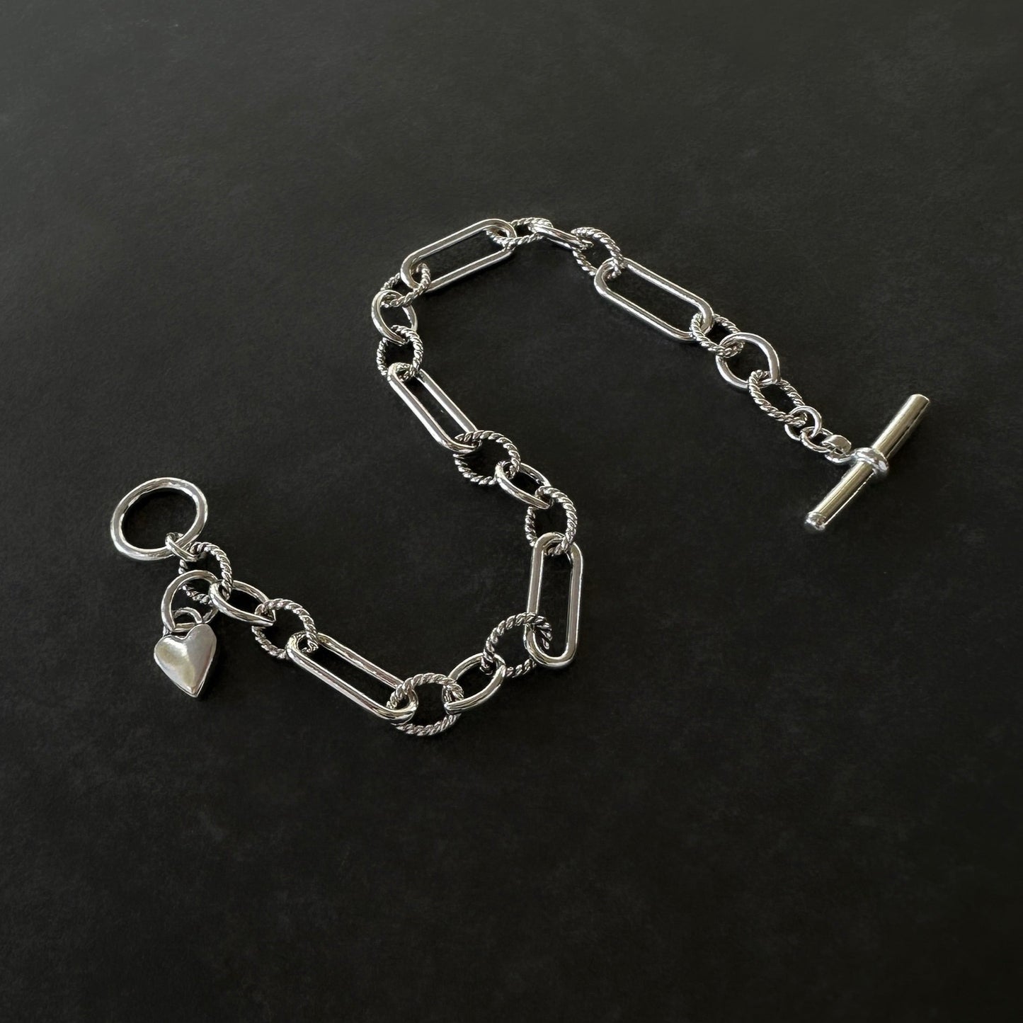 Silver chain bracelet with a heart charm on a black background