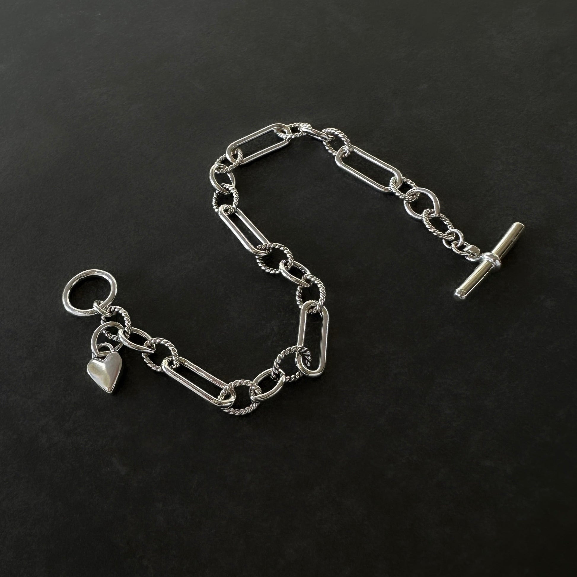 Silver chain bracelet with a heart charm on a black background