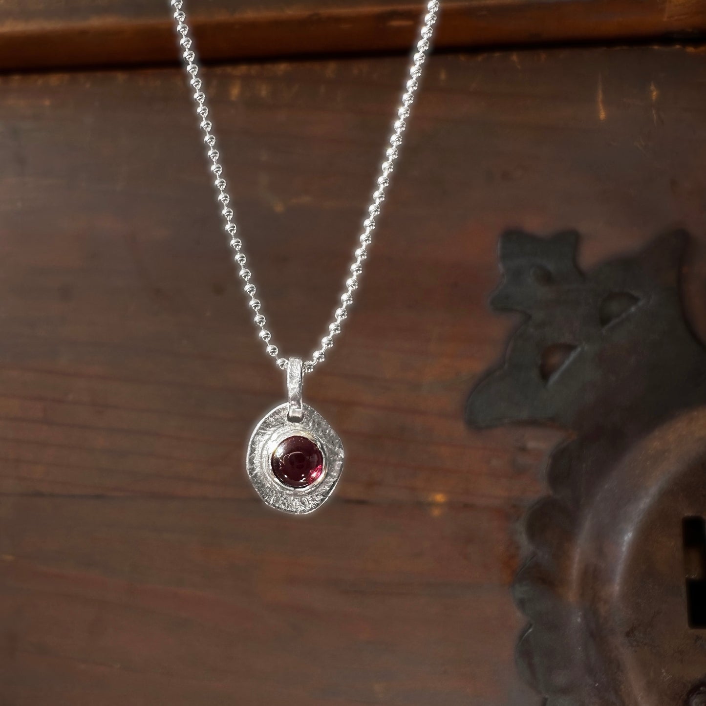 Silver necklace with a red garnet gemstone pendant on a wooden surface