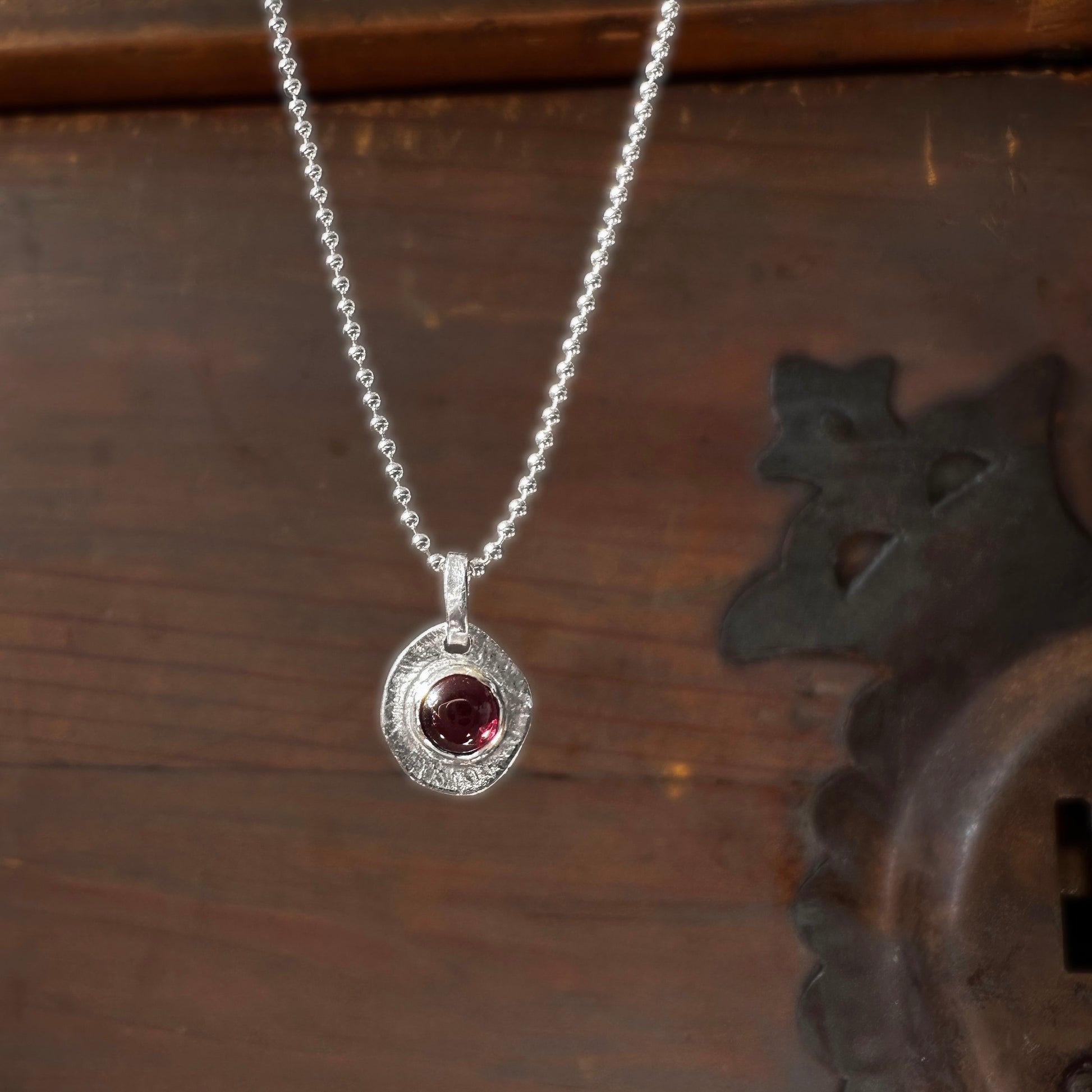 Silver necklace with a red garnet gemstone pendant on a wooden surface